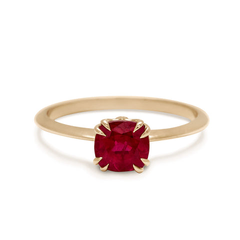 A solitaire cushion cut ruby ring with double claw prongs set in a knife edge yellow gold band.