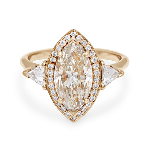 A three stone engagement ring with a marquise shape champagne diamond center stone surrounded by a white diamond pave halo with two white diamond trillion side stones set in yellow gold.