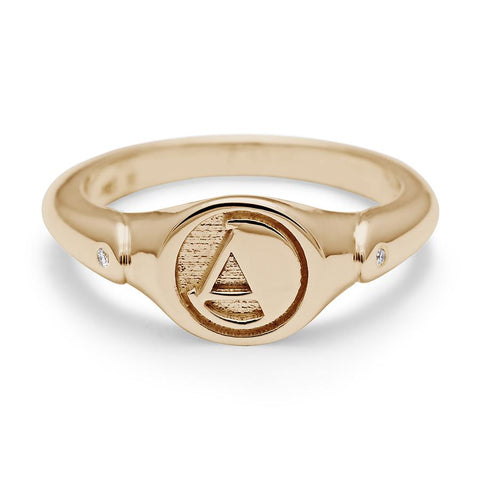 A monogrammed signet ring with an "A" on the front and two white diamond accents on either side and set in yellow gold.