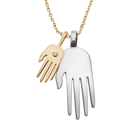 A large hand sterling sliver hand with a small yellow gold hand with a white diamond accent stone next to it on a yellow gold chain.