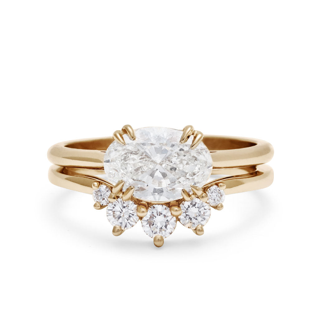 An east/west solitaire ring with an oval shape white diamond stone set in yellow gold set above a 5 white diamond curve band.