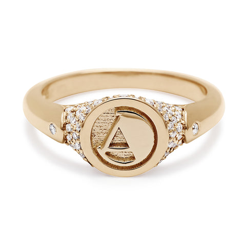 A monogrammed signet ring with an "A" on the front with white diamond pave around and two white diamond accents on either side and set in yellow gold.