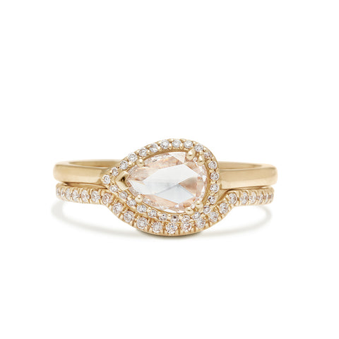 A pear shaped ring with a white diamond and white diamond halo set in yellow gold stacked above a scalloped white diamond yellow gold band.