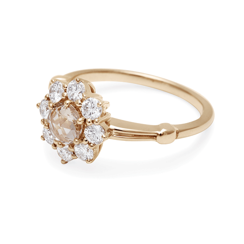 Angled view of a cluster engagement ring with a rose cut champagne diamond center stone and round white diamond stones surrounding it set in yellow gold. 3