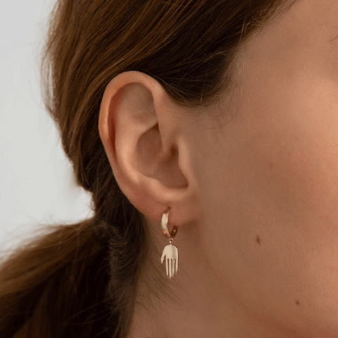 A hoop with a hand attached set in yellow gold on a light-complexion model's ear. 2
