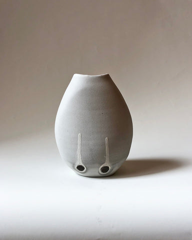 A ceramic pot in a blend of white and grey with two black dots at the bottom set on a grey background - Straight on View