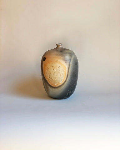 A ceramic pot in a blend of yellow and grey set on a tan background.