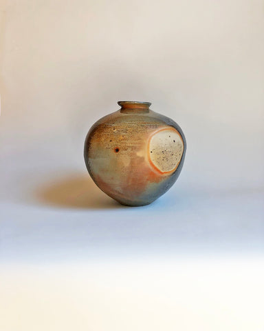 A ceramic pot in a blend of yellow, orange, and grey set on a tan background.