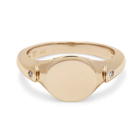 A solid gold signet ring with two white diamond accents on either side and set in yellow gold.