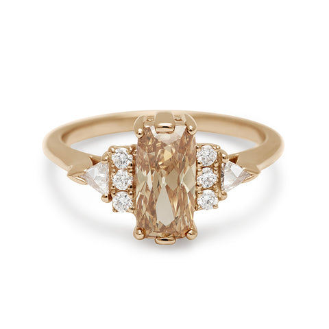 A cushion shape champagne diamond center stone ring with three round white diamonds on either and two white diamond trillions on the outer edges of each side set in yellow gold.