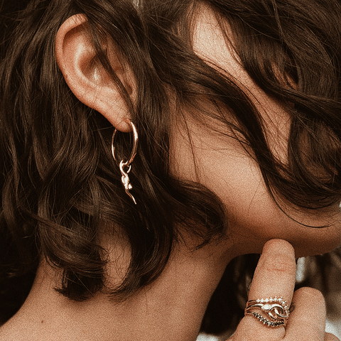 Side view of a female wearing A hoop earring with a serpent charm at the bottom set in yellow gold on a medium complexion model's ear with short brown hair. 2