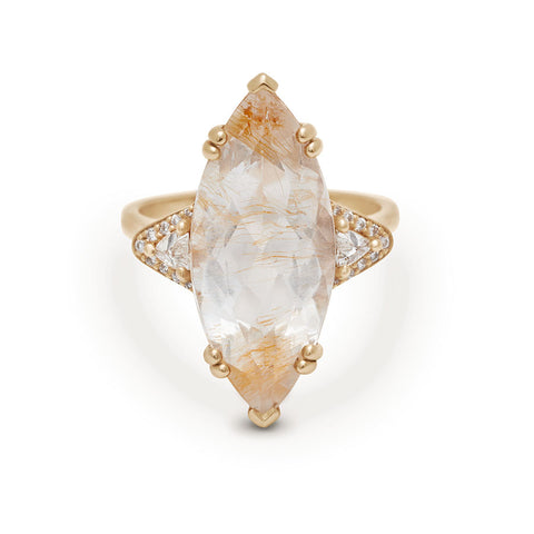 A three stone engagement ring with a marquise shape copper rutilated quartz center stone with two white diamond trillion side stones with white diamond pave halos around them set in yellow gold.