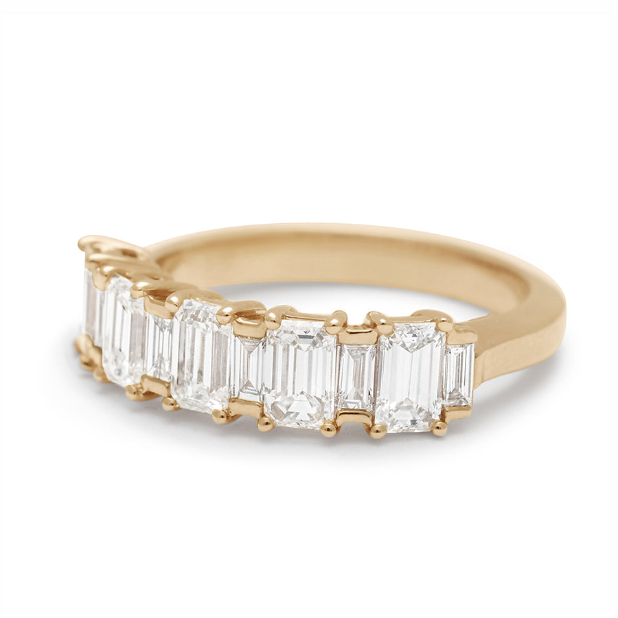 Angled view of a band with alternating emerald and baguette cut white diamonds set in yellow gold.