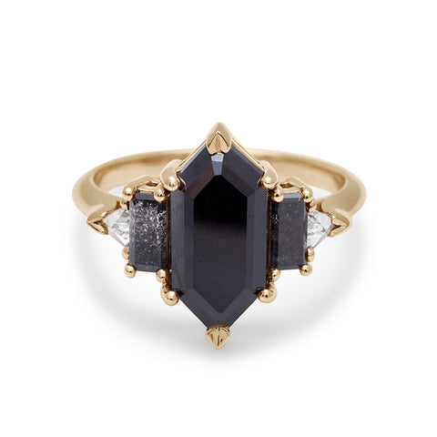 A ring with a hexagonal shaped black diamond center stone with one baguette black diamond and one white diamond trillion on either side set in yellow gold.