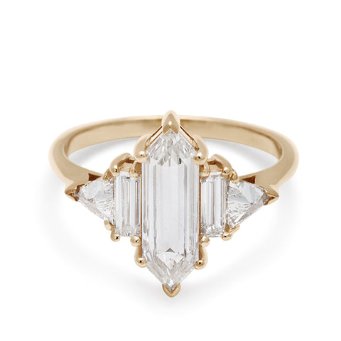 A ring with a hexagonal shaped white diamond center stone with one baguette white diamond and one white diamond trillion on either side set in yellow gold.