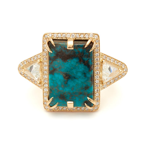 An emerald shaped turquoise set between two white diamond trillion side stones and all encircled in white diamond pave halo set in yellow gold.