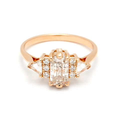 An emerald cut grey diamond center stone ring with three round white diamonds on either and two white diamond trillions on the outer edges of each side set in yellow gold.