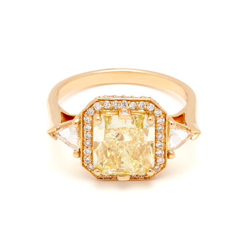 A three stone engagement ring with an radiant cut yellow diamond center stone surrounded by a white diamond pave halo with two white diamond trillion side stones set in yellow gold.
