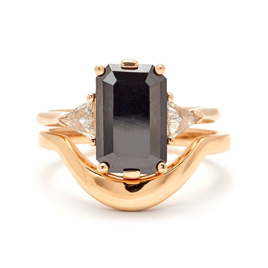 A three stone engagement ring with an 11x7mm black diamond center stone with white diamond trillions set in yellow gold and stacked on top of a yellow gold solid gold curve band.