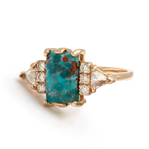 A emerald shape turquoise center stone ring with three round white diamonds on either and two white diamond trillions on the outer edges of each side set in yellow gold.