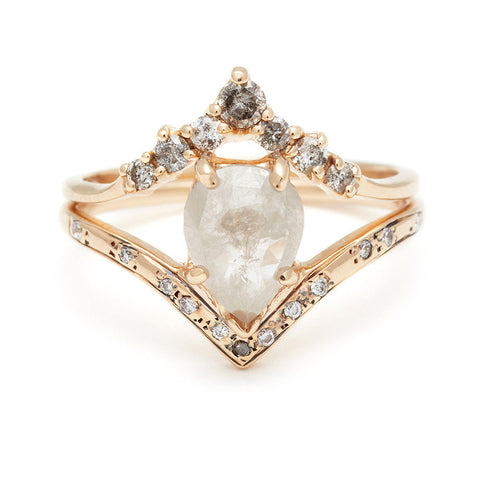 A pear shaped grey diamond engagement ring with grey diamond pave on the band stacked beneath a grey diamond chevron band all set in yellow gold.