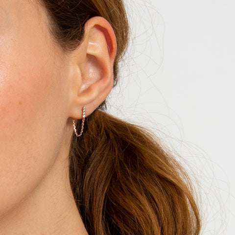 A single earring with four white diamonds with a chain connecting to the ear back set in yellow gold on a light-complexion ear., White Gold, Rose Gold, Yellow Gold 3