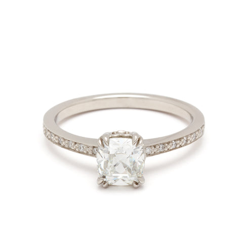 A solitaire ring with a knife edge white diamond with white diamond pave on either side set in white gold.