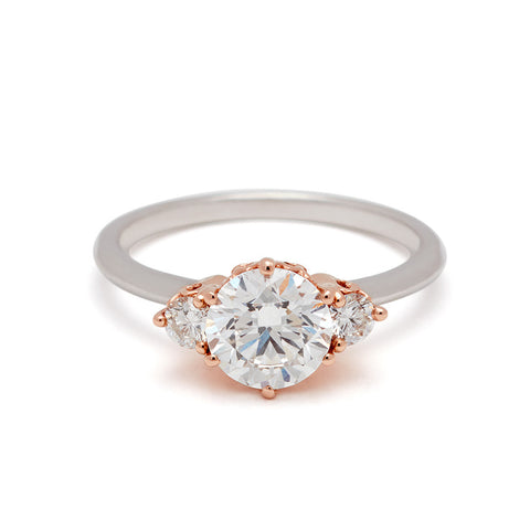 A three stone engagement ring with a round shape white diamond center stone with two white diamond round side stones set in a rose gold basket and a white gold band.