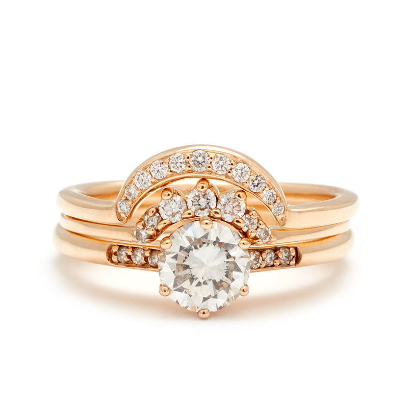 A solitaire ring with a round white diamond with white diamond pave on either side set in yellow gold below a 7 white diamond tiny curve band and a crescent shaped white diamond band.