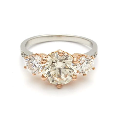 A three stone engagement ring with a round shape champagne diamond center stone with two white diamond round side stones set in a rose gold basket and a platinum band.