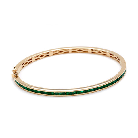 A bracelet with a line of emeralds set around the band set in yellow gold.