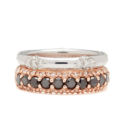 A straight band with 5 clusters white diamond band set in white gold stacked above a band with round black diamonds in a 3/4 pave around a rose gold band with white diamond accents on both top and bottom. 9