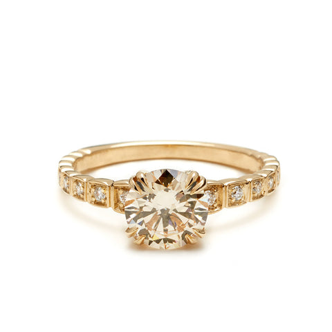 A solitaire ring with a brilliant cut champagne diamond with white diamond pave around the band set in yellow gold.